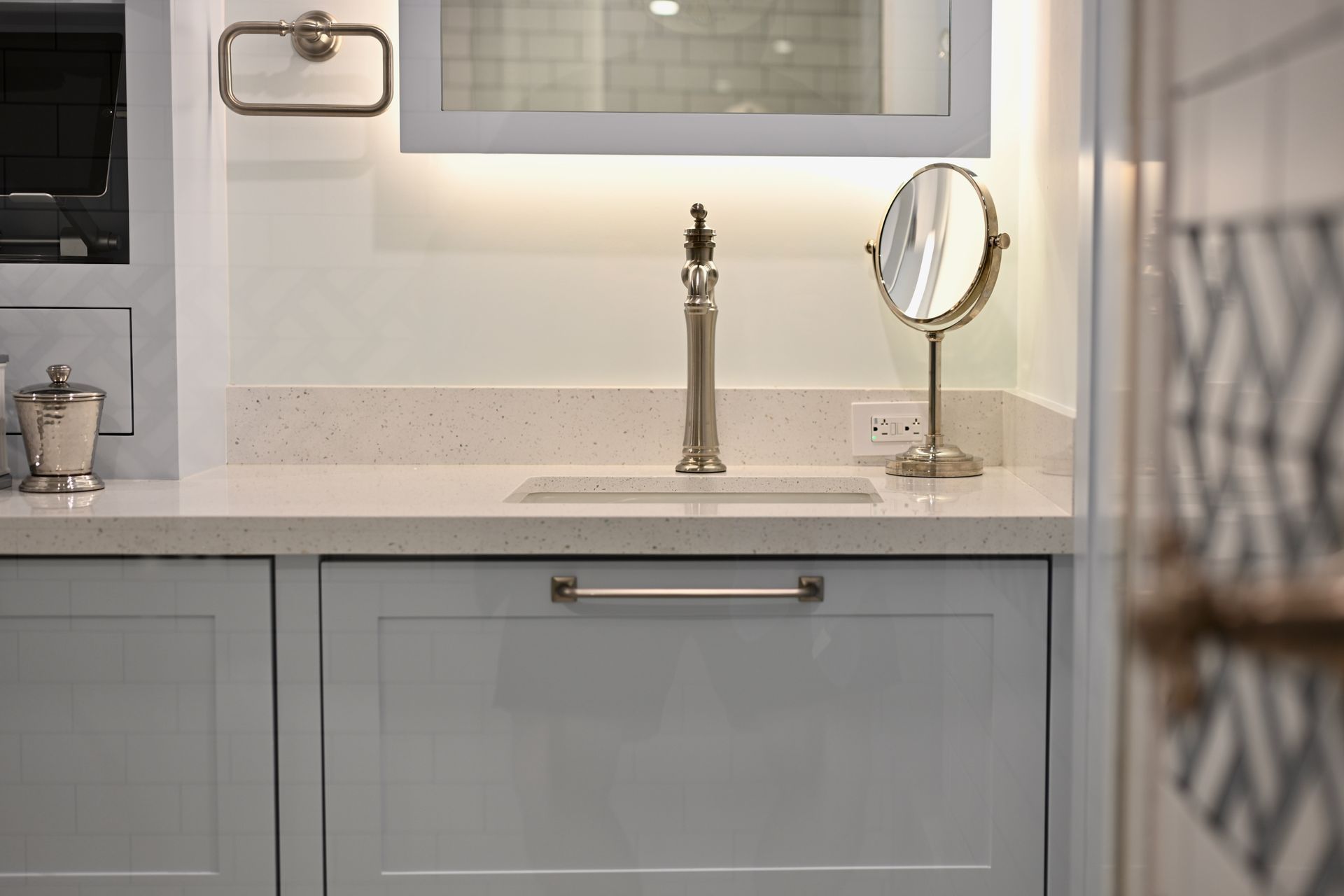 Bathroom vanity with white countertop, gray cabinet, mirror, and gold faucet details