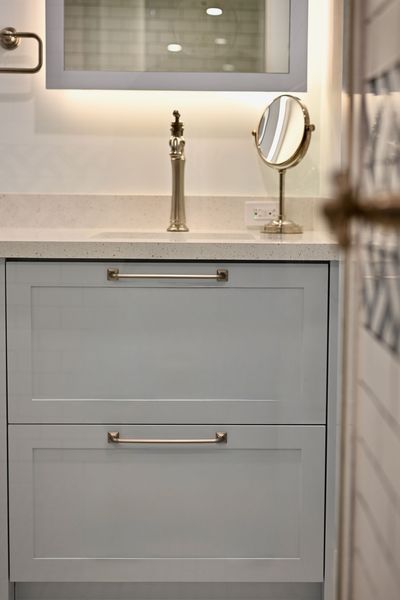 Light gray bathroom vanity with sink, gold faucet, and round tabletop mirror under a window