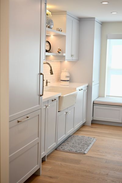 Bright, narrow kitchen with white cabinets, sink, wood floor, and window seat near the window.