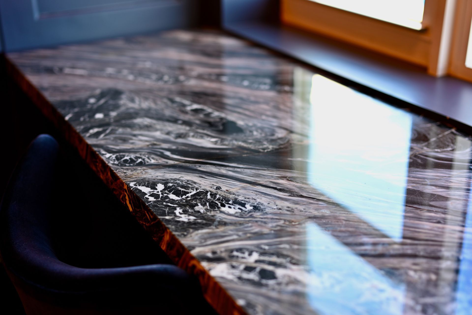 Marble tabletop by a sunlit window, with glossy reflections and a dark chair edge nearby