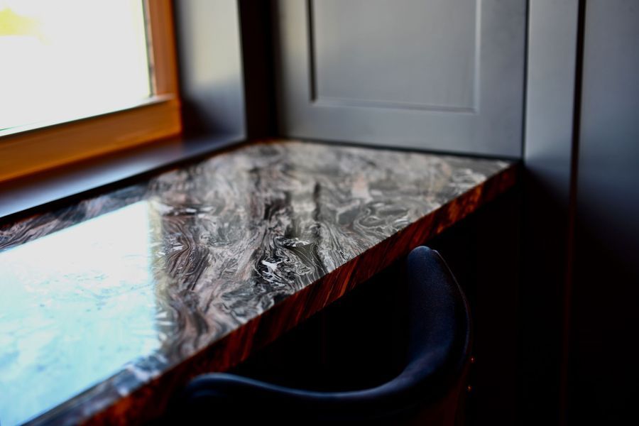 Marble-top desk by a window with a dark chair in a modern room