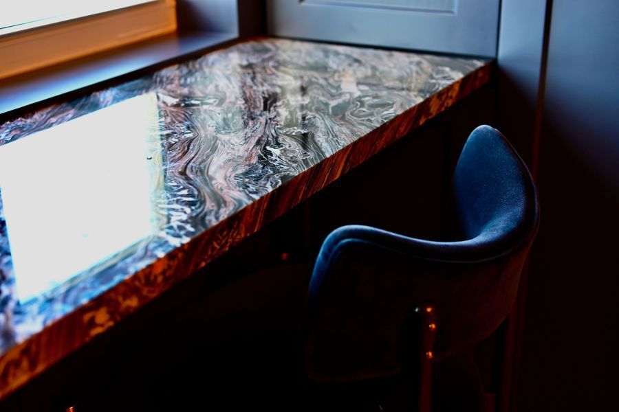Marbled table by a sunlit window with a blue chair in a dim room