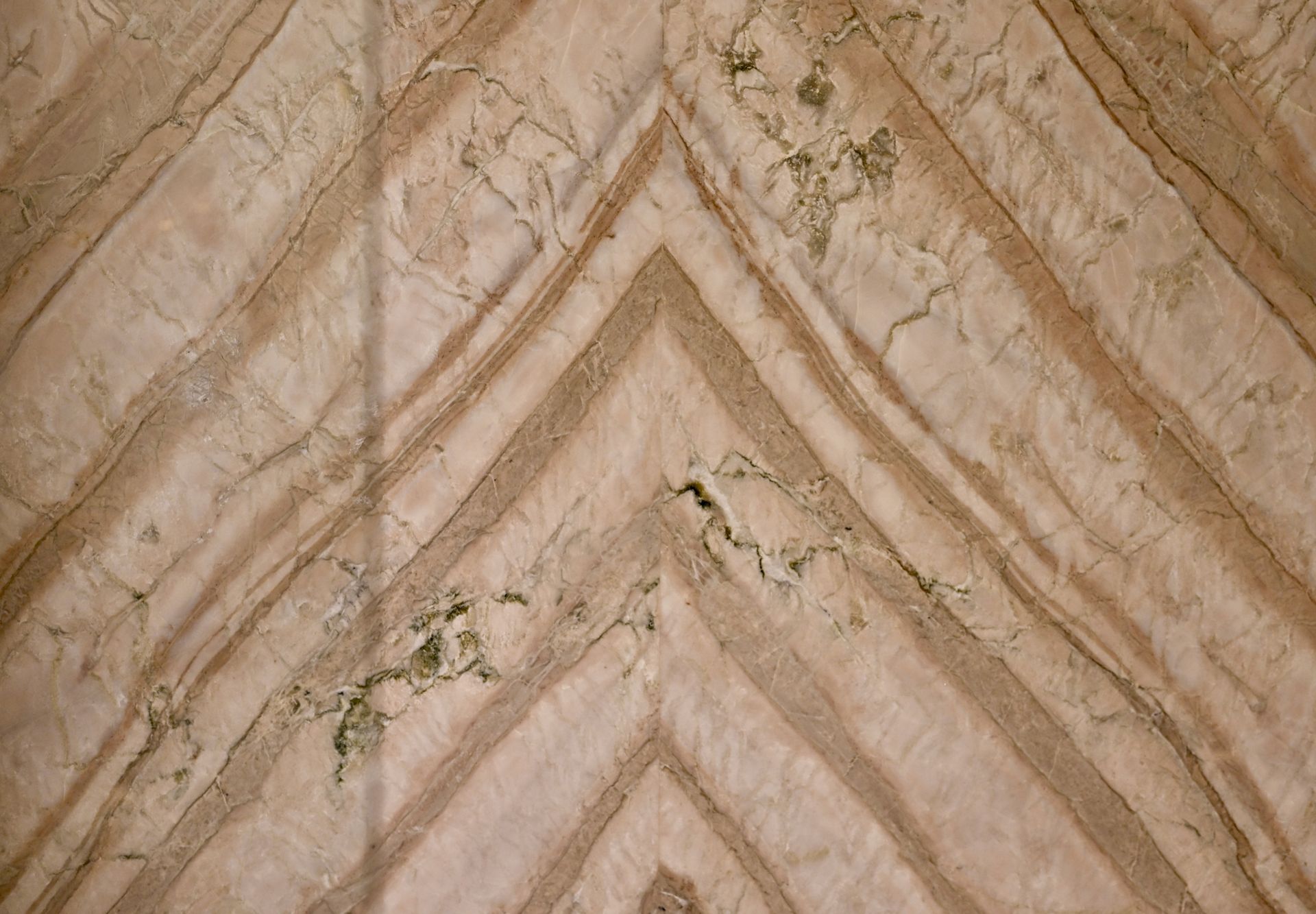 Close-up of a beige herringbone tile surface with visible cracks and stains