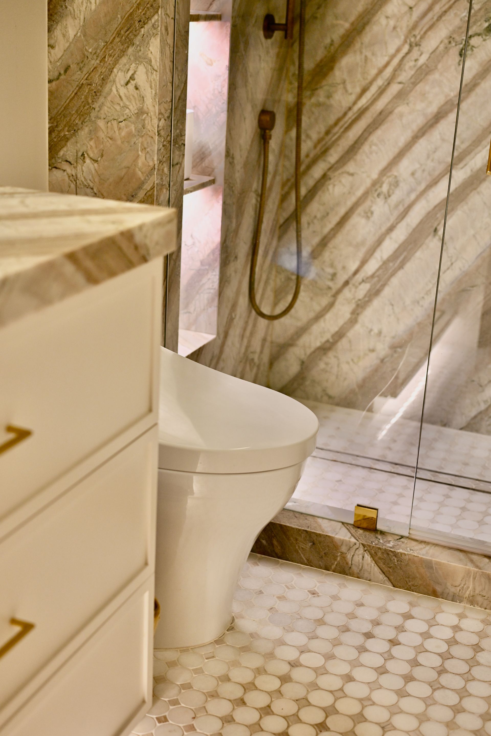 Small bathroom with white toilet, marble shower wall, and hexagon tile floor