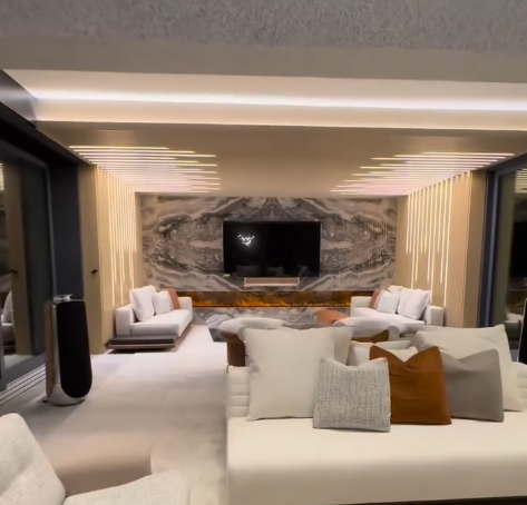 Modern living room with white sofas, stone fireplace wall, TV, and warm recessed lighting