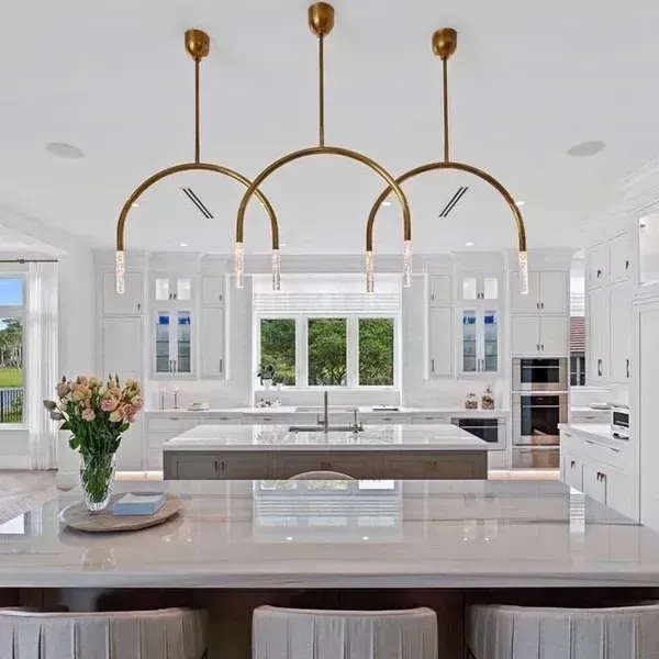 Bright white modern kitchen with a large island, gold pendant lights, and flowers on the counter