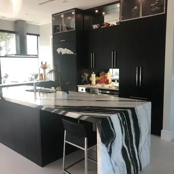 Modern black kitchen with marble island and a bar stool by a bright window.