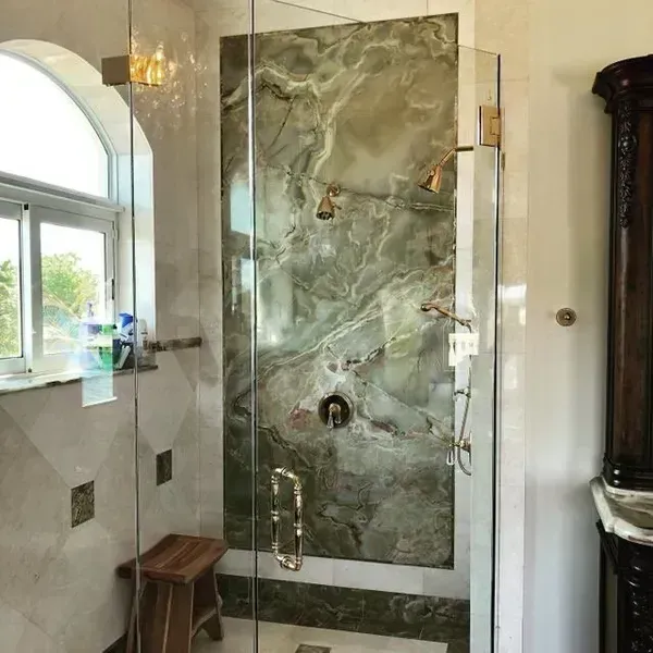 Glass shower with green marble tile in a bright bathroom