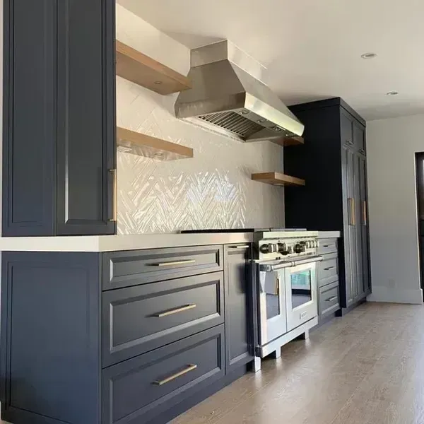 Modern kitchen with dark navy cabinets, stainless steel range, and light wood shelving