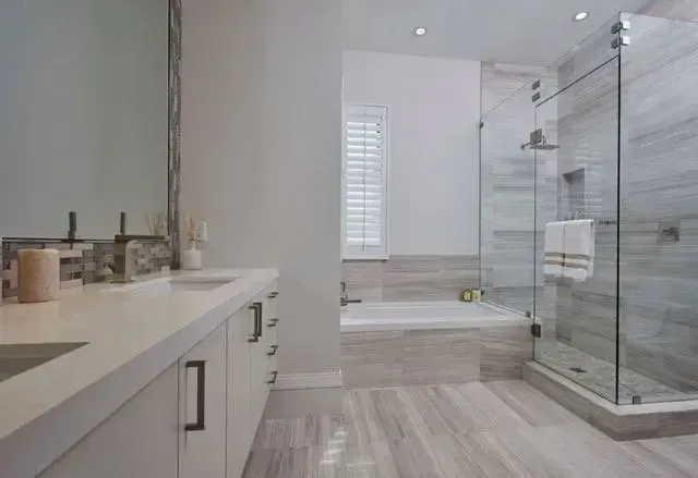 Modern white bathroom with double vanity, glass shower, and freestanding tub near a window.