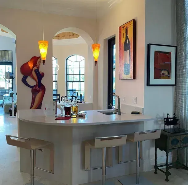 Modern kitchen with white island, pendant lights, wall art, and arched doorway to dining area