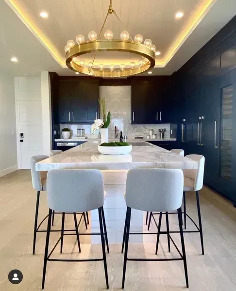 Modern dining room with dark blue cabinets, white table, and gold chandelier in a bright interior.