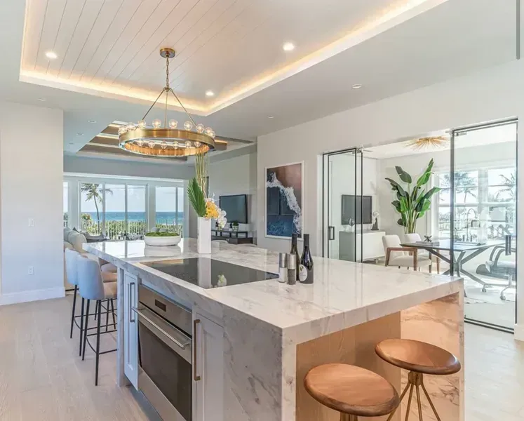 Modern kitchen with marble island, brass pendant light, and ocean-view dining area