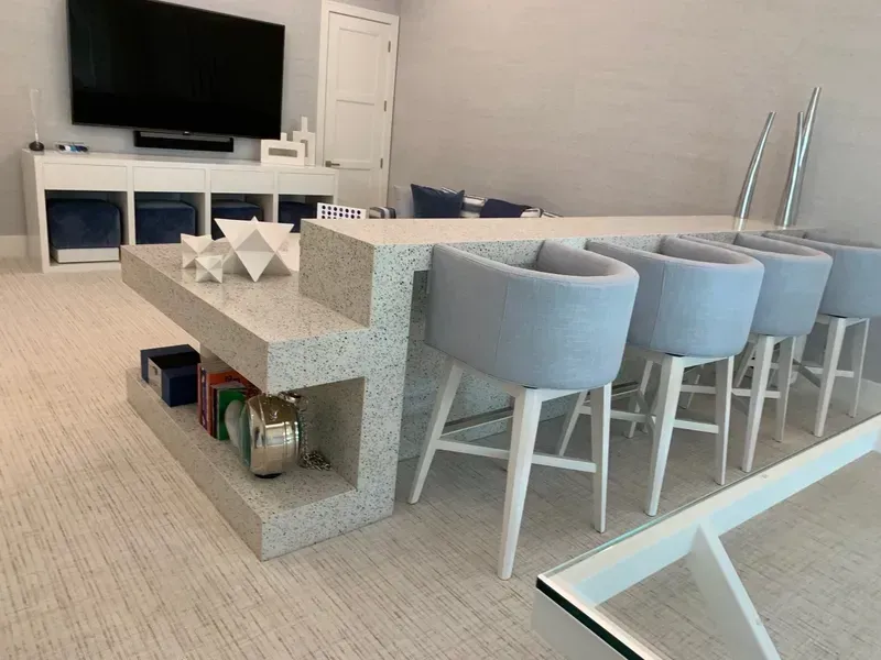 Modern living room with gray bar stools at a kitchen island, TV, and light carpet flooring
