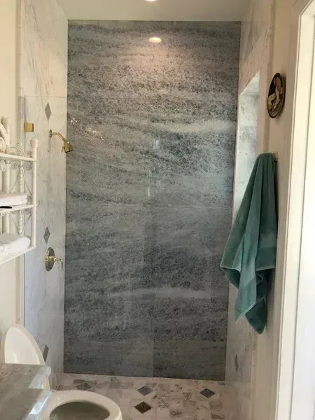 Small bathroom with a tiled shower, white walls, and green towels hanging on the right.