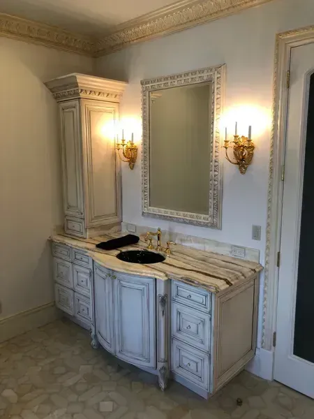 Elegant bathroom vanity with marble countertop, mirrored cabinet, and gold wall sconces in a cream-colored room