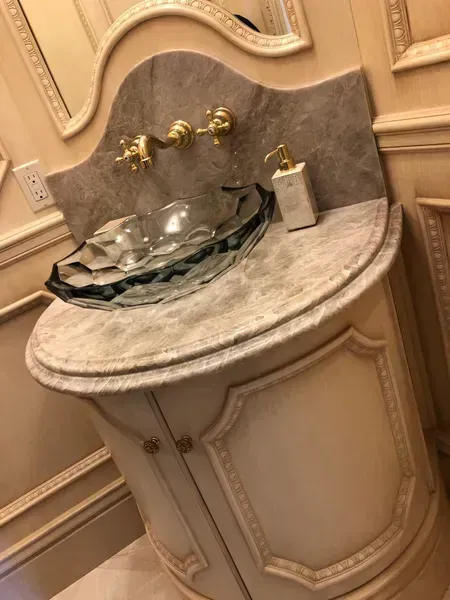 Elegant cream marble bathroom vanity with brass faucets and a glass tray on the sink countertop