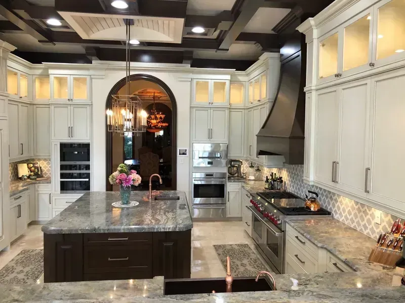 Bright luxury kitchen with white cabinets, marble island, stainless appliances, and mosaic backsplash