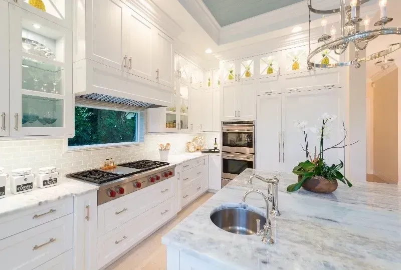 Bright white modern kitchen with marble island, stainless sink, and large windows