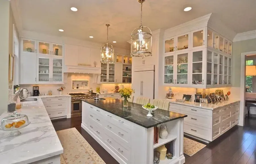 Bright modern kitchen with white cabinets, dark island, marble countertops, and hanging lantern lights
