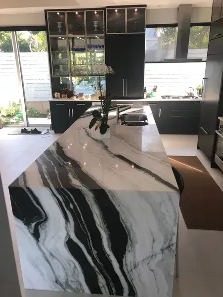 Modern kitchen with a marble waterfall island, black cabinetry, and large windows.