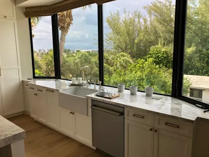 Bright kitchen with marble countertop and large windows overlooking lush greenery and ocean view