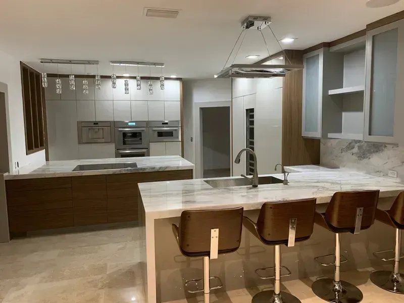 Modern kitchen with white island, brown bar stools, stainless appliances, and pendant lights