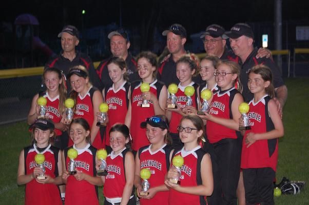 Youth baseball team in red jerseys holding trophies after a night game