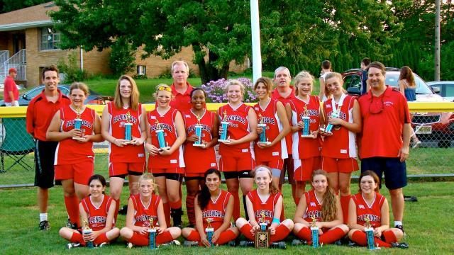 Soccer team in red uniforms posing with trophies on a field