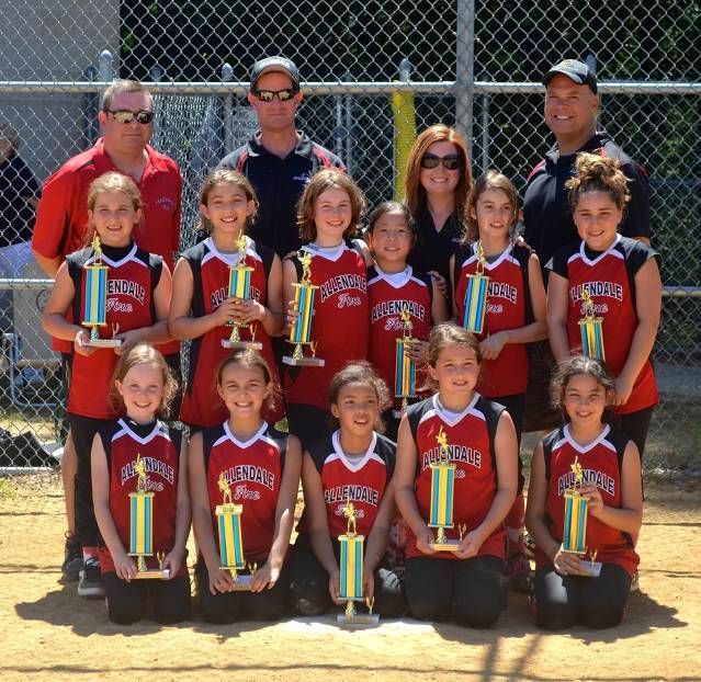 Youth sports team posing with trophies in front of a chain-link fence.