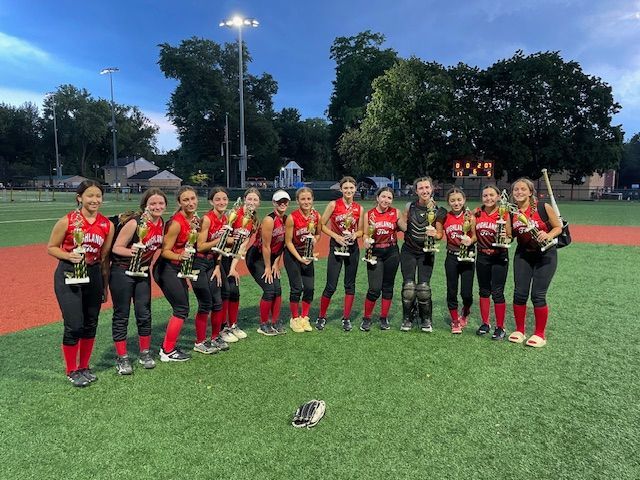 Girls’ lacrosse team in red and black uniforms posing on a turf field at dusk