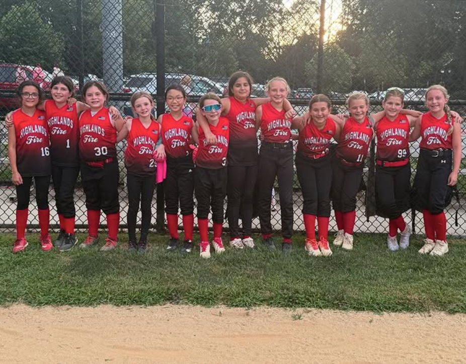 Youth softball team in red uniforms posing in a row on a field at sunset.