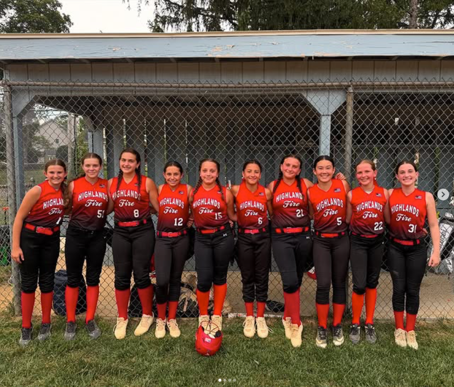 Ten softball players in orange jerseys and black pants posing on a field in front of a chain-link fence
