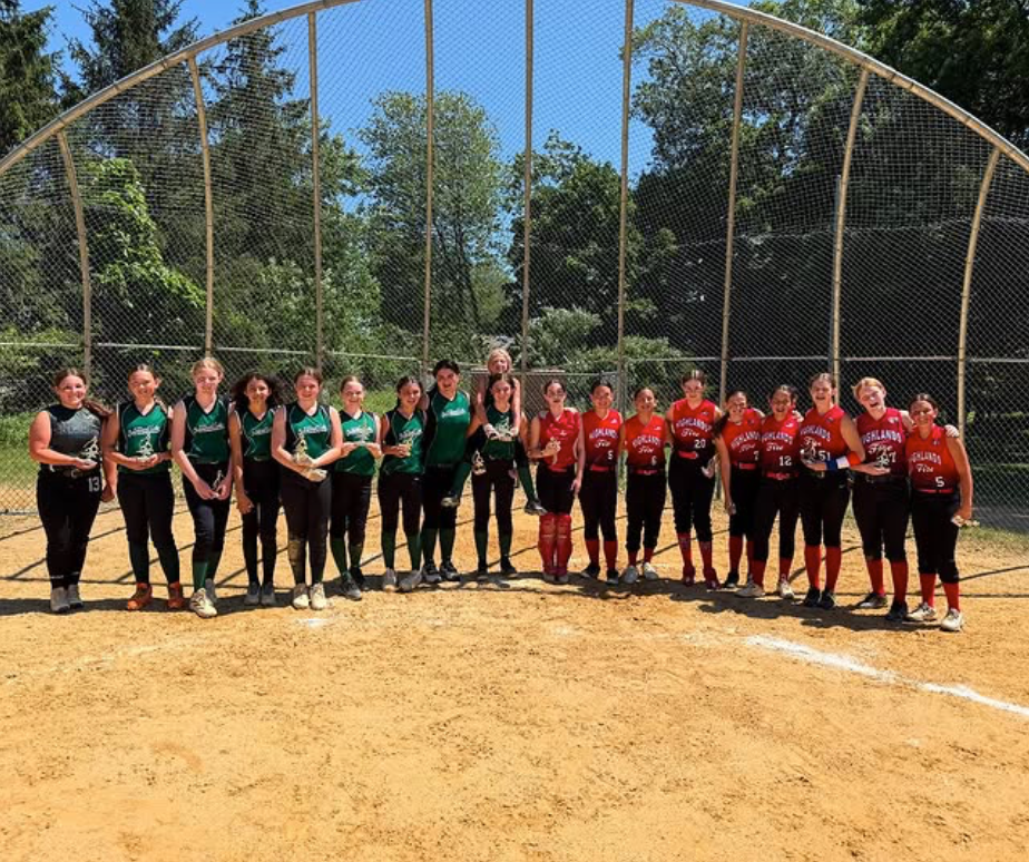 Two teams in green and red uniforms lined up on a softball field with a chain-link backstop
