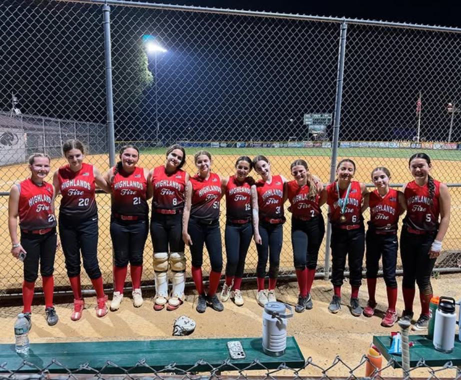 Softball team in red and black uniforms posing together on a field at night.