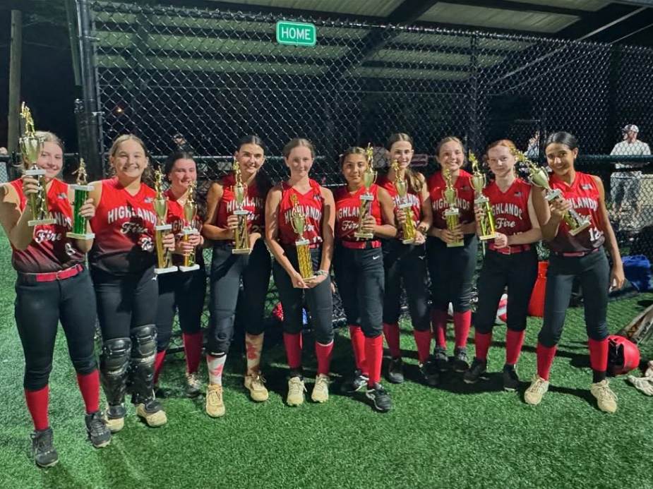 Youth softball team in red uniforms posing with trophies on an indoor turf field