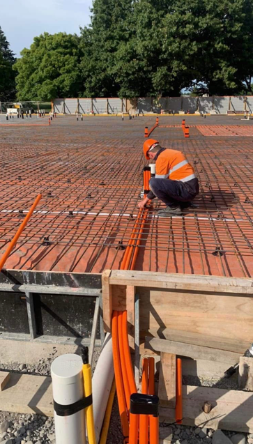 Construction worker installing orange conduit on a rebar grid at a construction site.