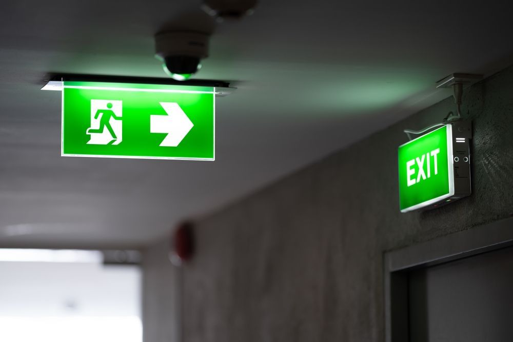 White emergency light with two spotlights on a blue wall, plugged into an outlet.