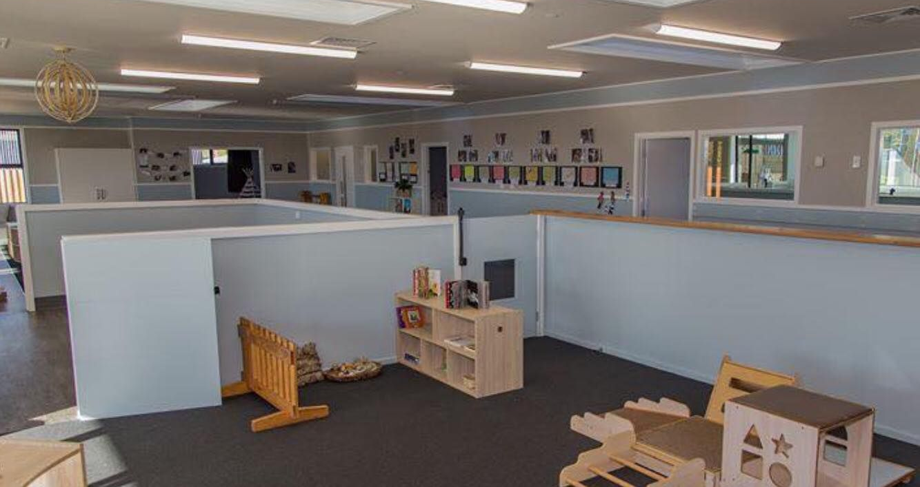 Daycare room with cubicle walls, natural wood furniture, and overhead lighting.