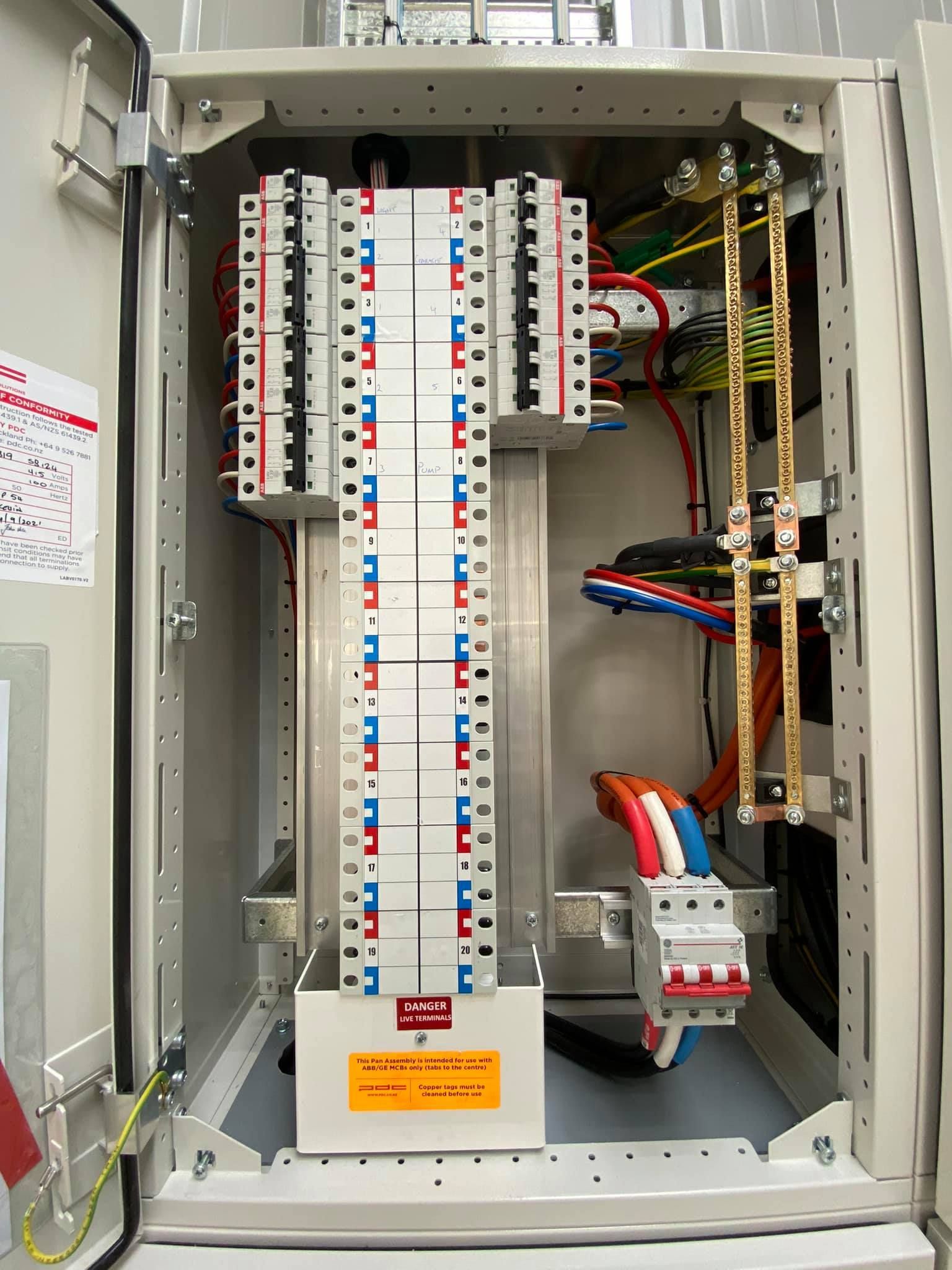 Electrical panel with circuit breakers, wires, and busbars inside a metal cabinet.