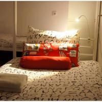 Cozy bed with patterned white bedding, red pillows, and a lit reading lamp in a softly lit bedroom