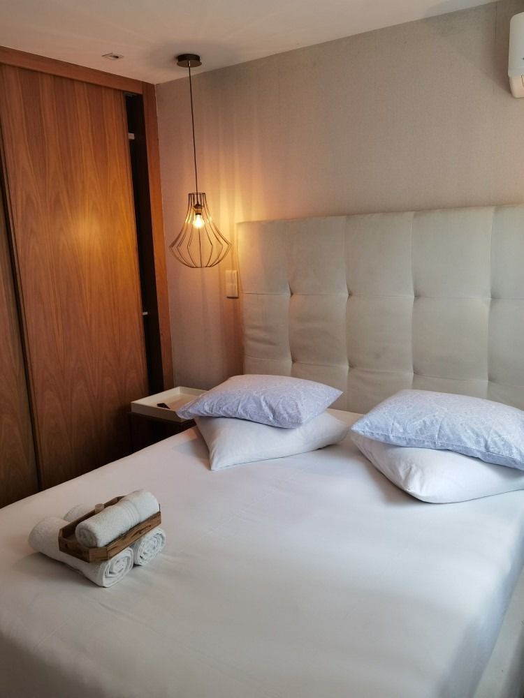 Neat bedroom with a white bed, tufted headboard, wooden wardrobe, and warm hanging lamp.
