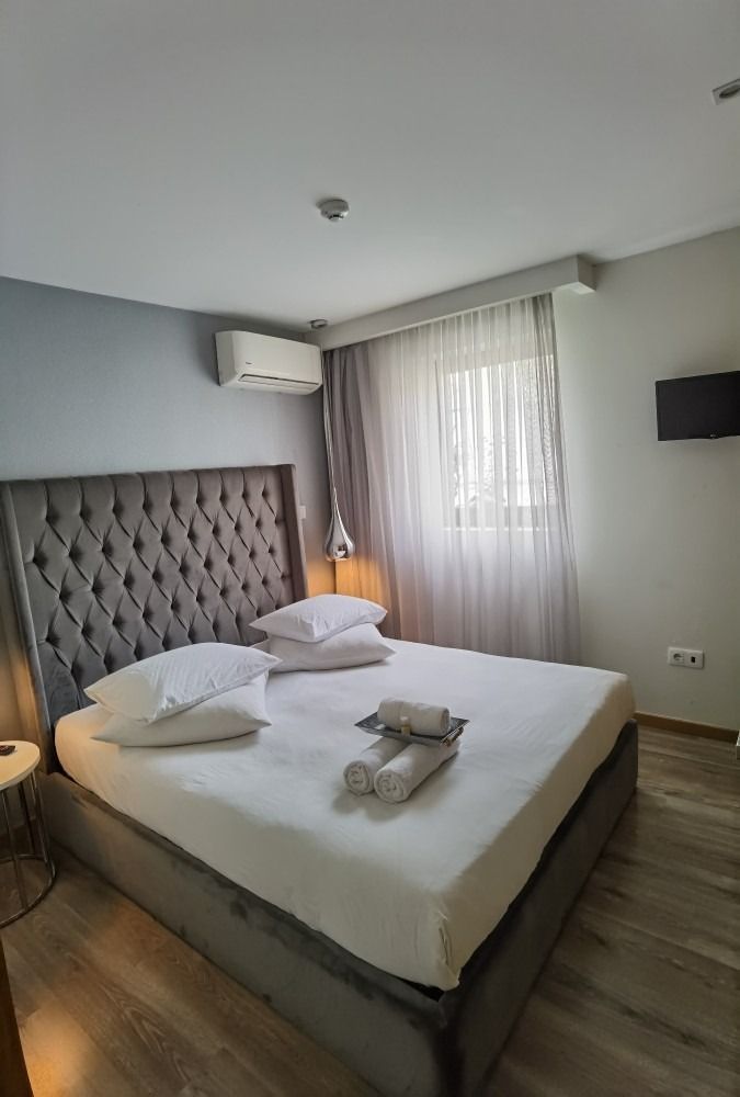 Modern bedroom with a large bed, tufted headboard, bedside lamp, window curtains, and wall-mounted TV