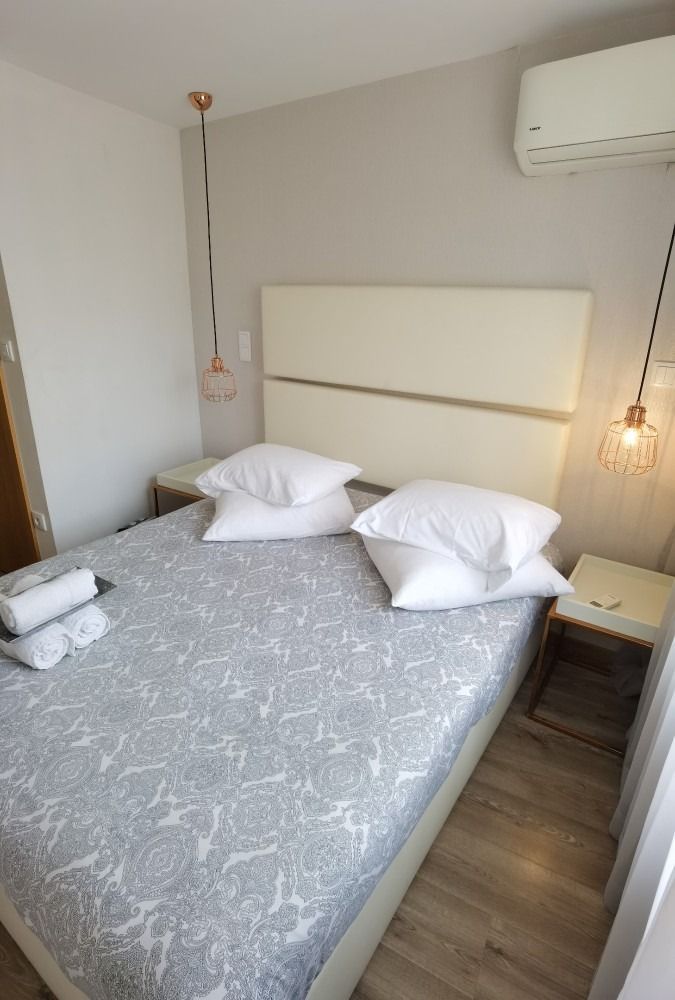 Small bedroom with double bed, gray bedding, white pillows, wall lights, and air conditioner