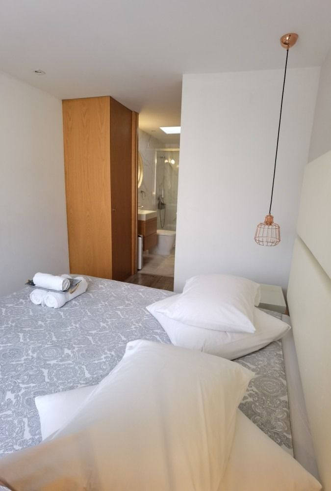 Small bedroom with unmade bed, white bedding, and an open doorway to a bathroom.