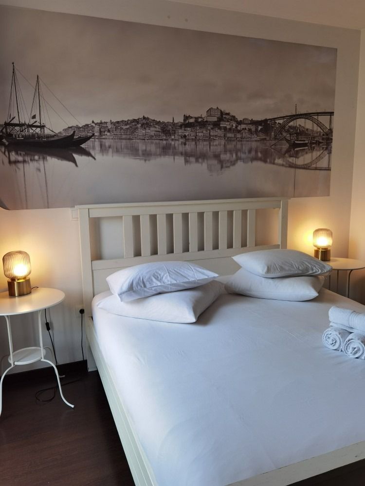 Neatly made bed in a cozy bedroom with bedside lamps and a large wall art panel