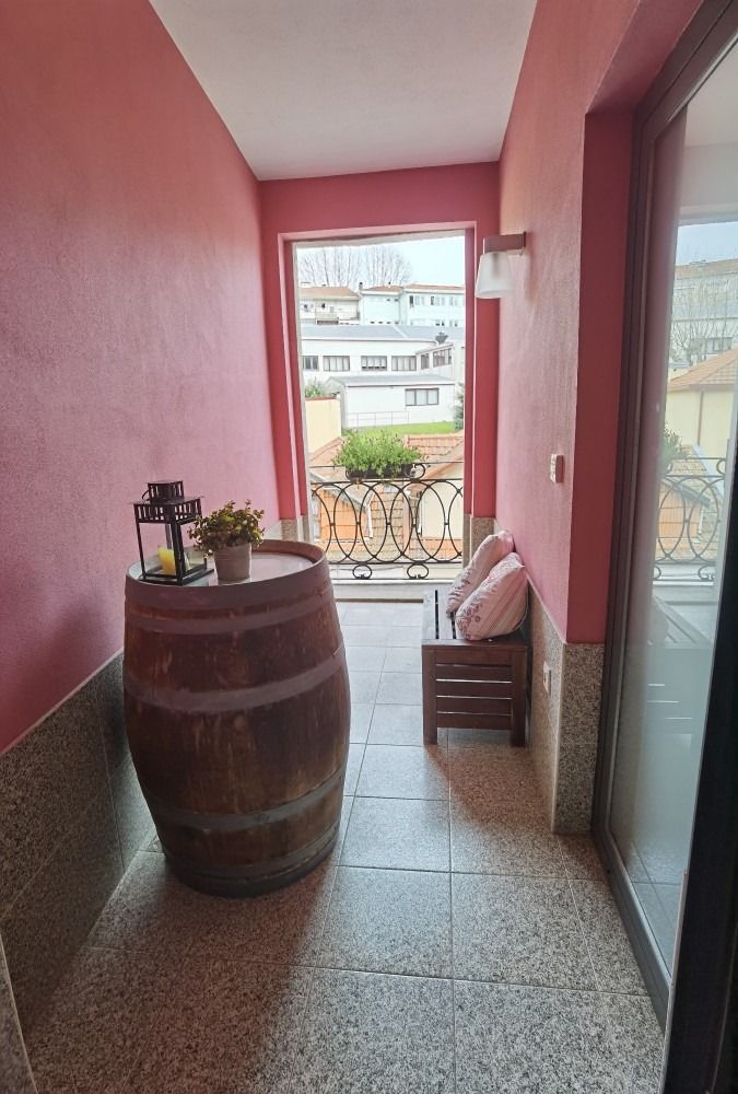 Narrow pink balcony with a wooden barrel table, chair, and open view of neighboring buildings