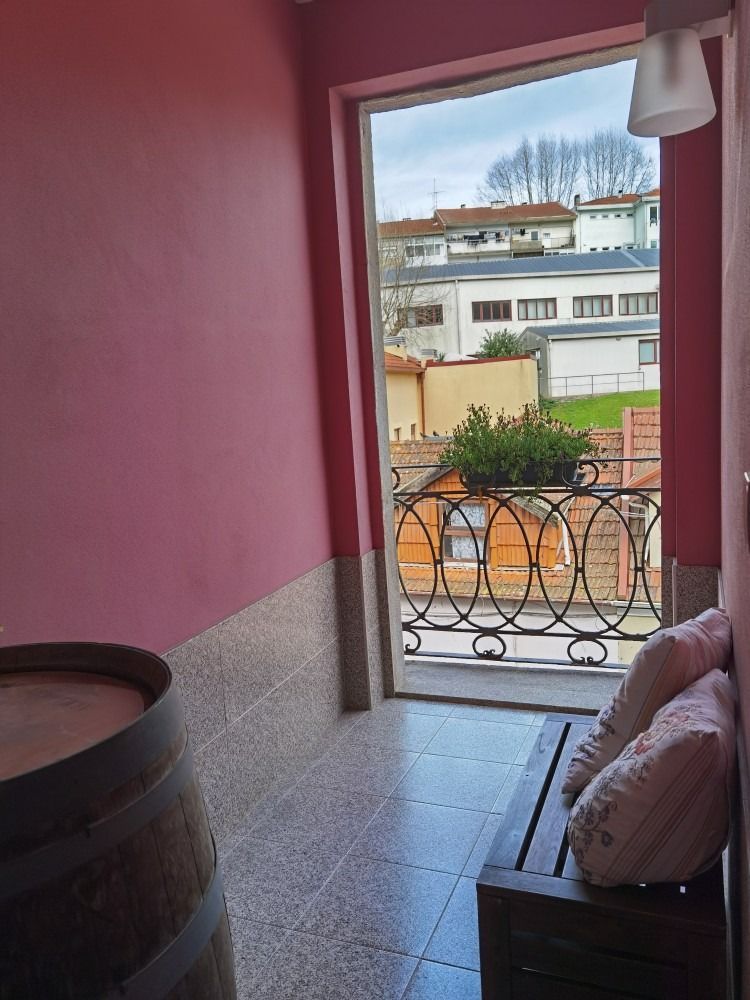 Pink-walled balcony with a tiled floor, open doorway, and a view of buildings and flowers outside.