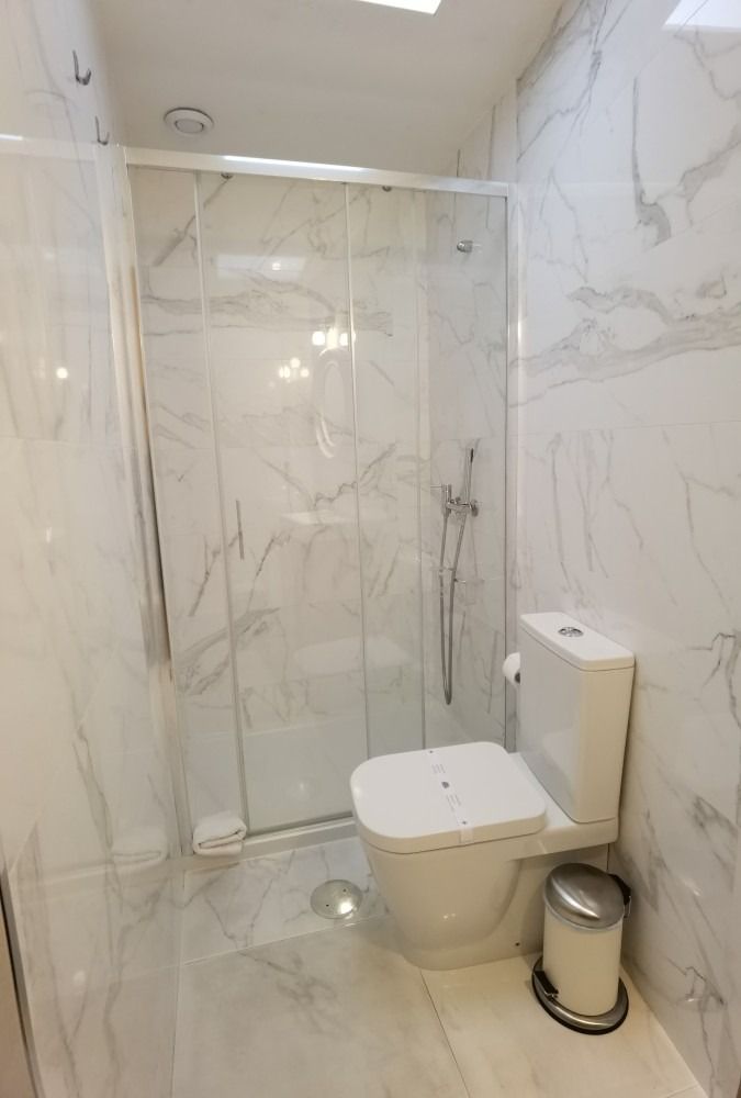 Compact tiled bathroom with a glass shower, wall-mounted toilet, and toilet paper holder.