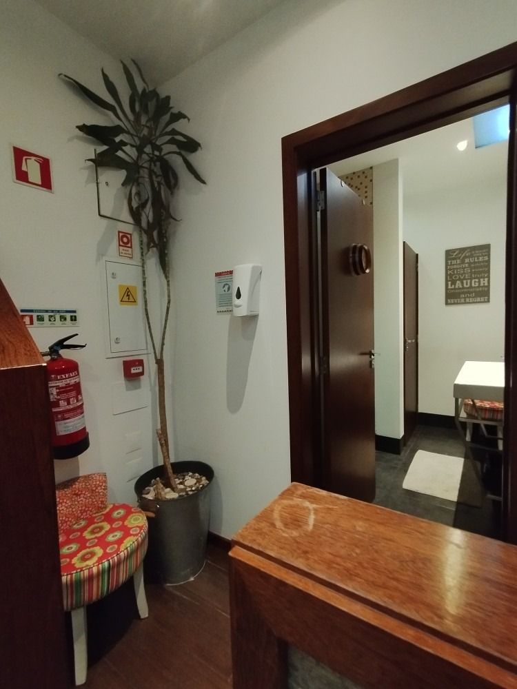 Interior hallway with a wooden bench, potted plant, red fire extinguisher, and open doorway to a restroom.
